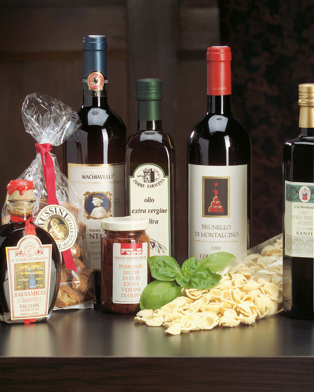 Stillleben mit italienischen Weinflaschen, Olivenöl, Aceto Balsamico, eingelegten Tomaten, Cantuccini und Orecchiette